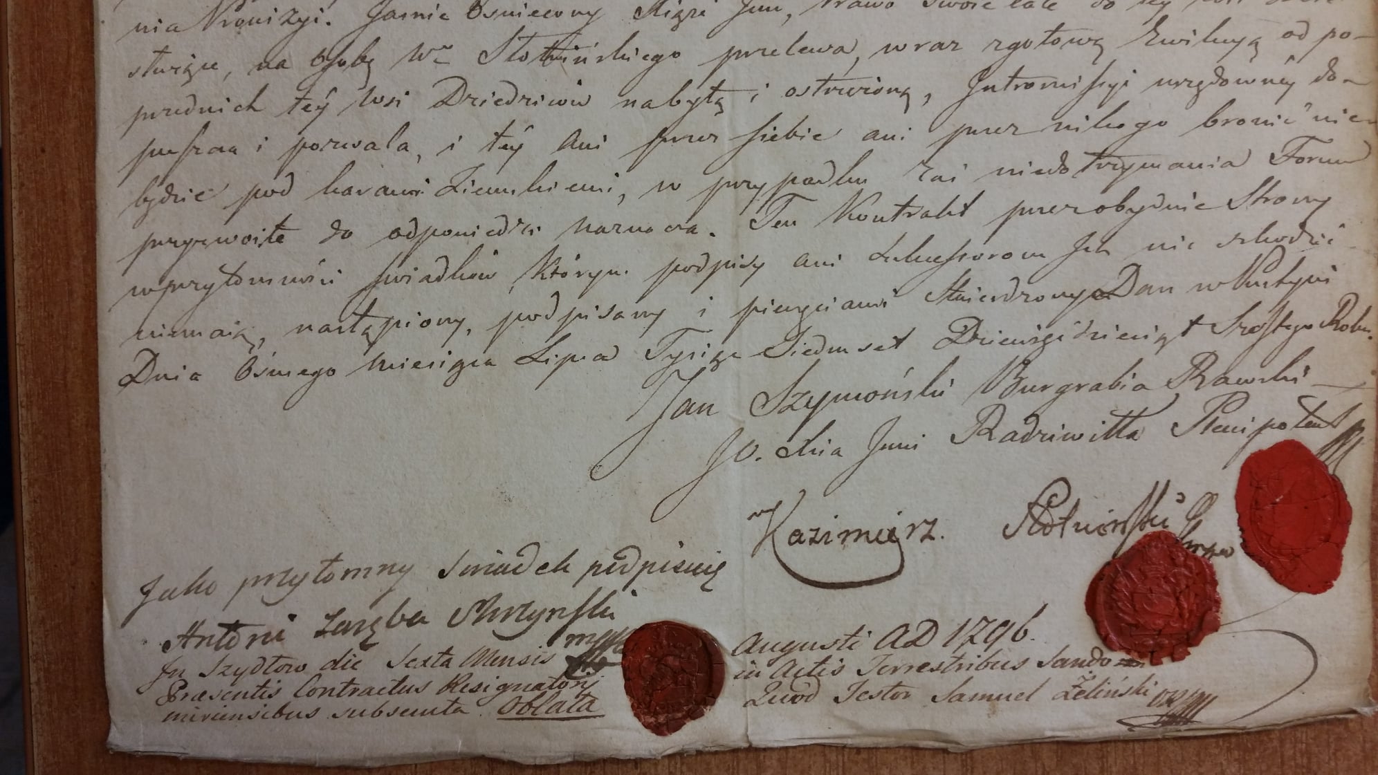 Close-up of an 18th-century Polish nobility deed with handwritten text, signatures including "Jan Szymoński" and "Kazimierz", and two red wax seals — dated August 1796.